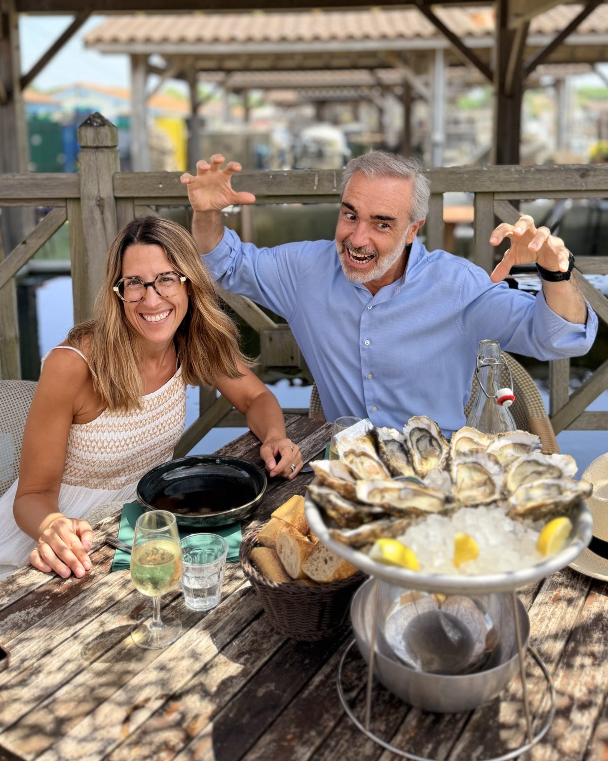 David Aragón y Pilar sonriendo en una mesa al aire libre con ostras, pan y una copa de vino