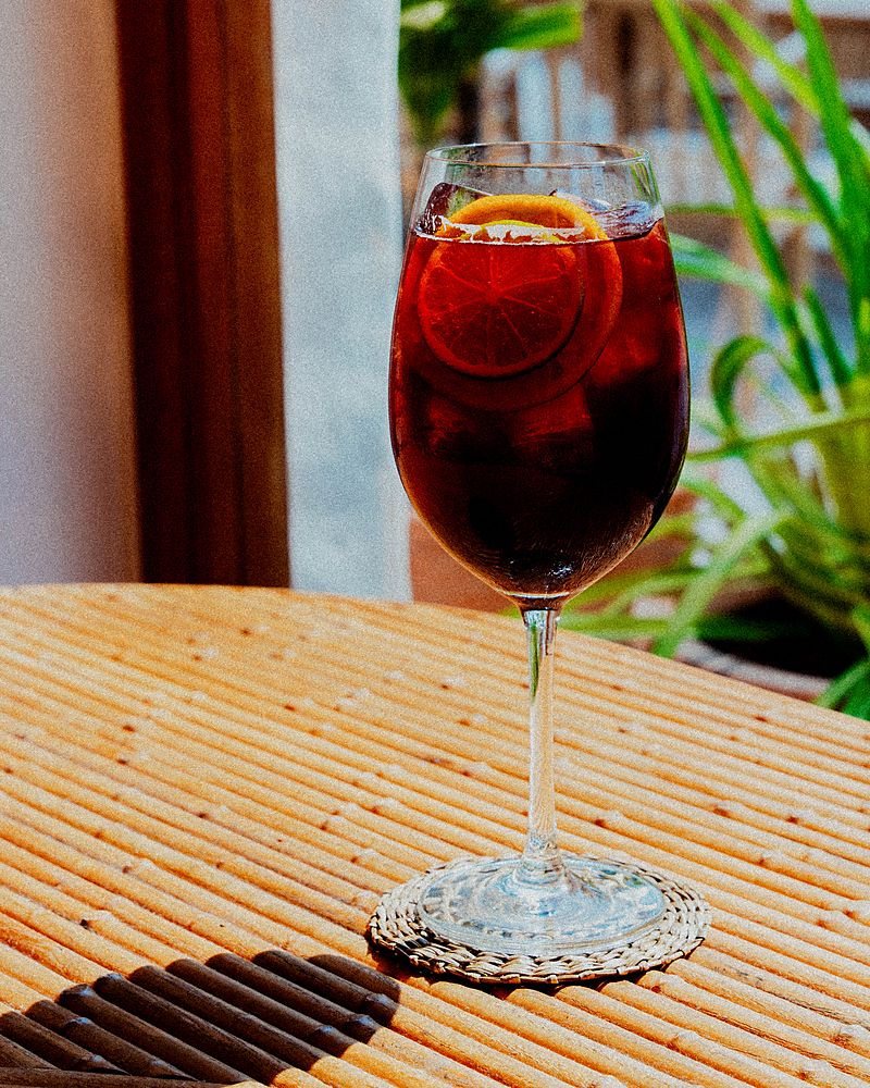 Copa de sangría con hielo y rodaja de naranja sobre una mesa al sol