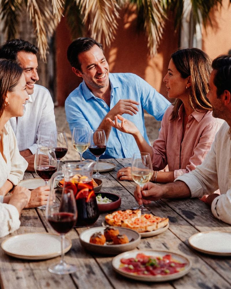 Grupo de amigos riendo alrededor de una mesa con vino y tapas