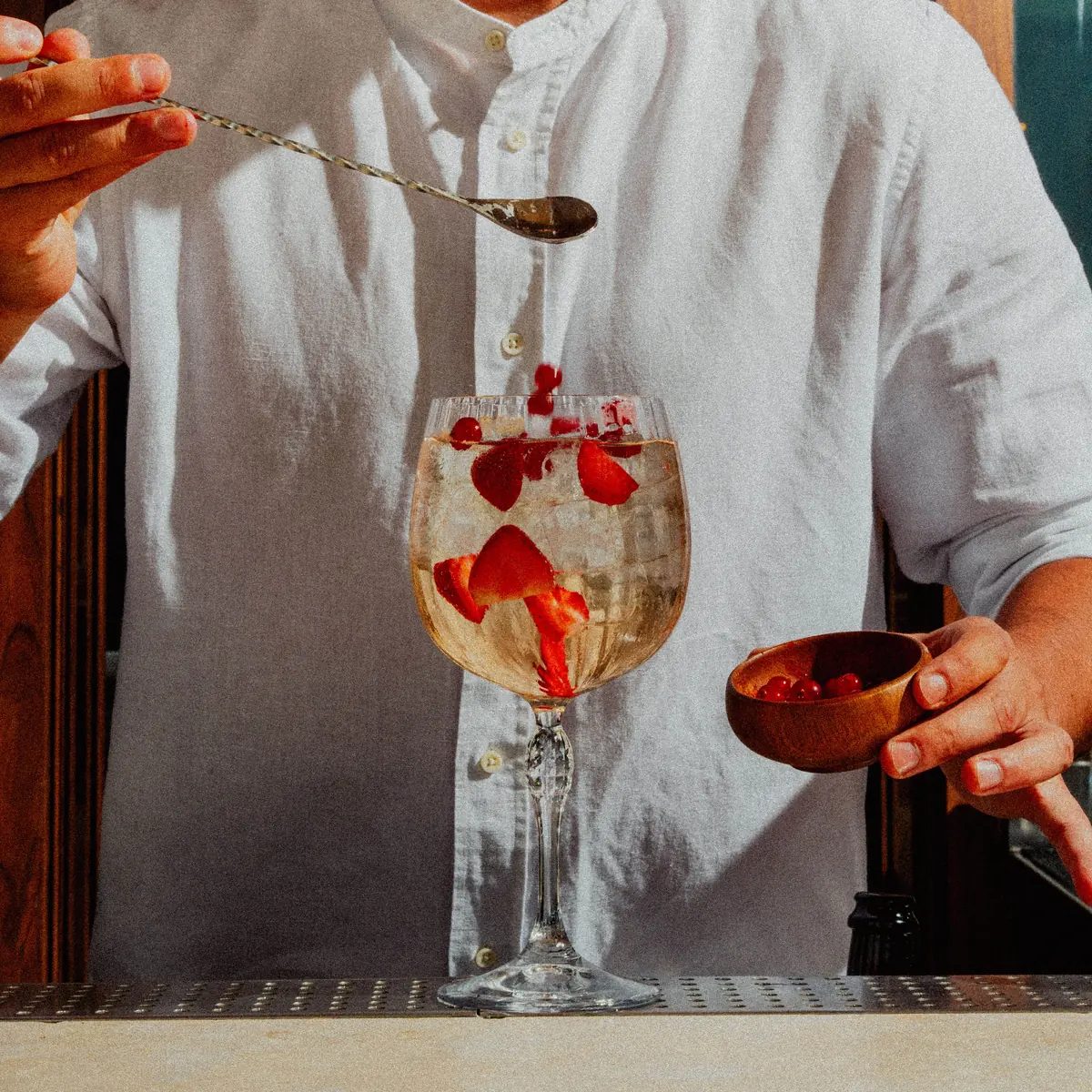 Bartender añadiendo grosellas a una copa de sangría rosada con fresas